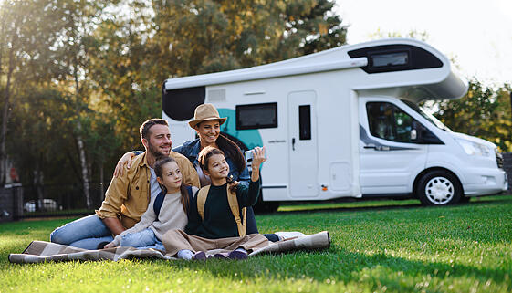 Happy young family with two children ltaking selfie with caravan at background outdoors.
