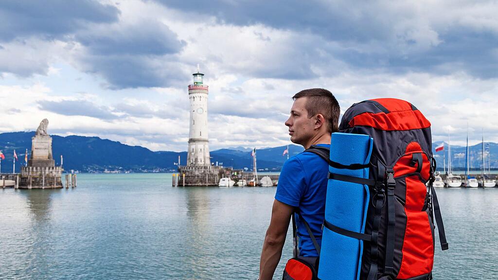 Junger Backpacker vor der Hafeneinfahrt in Lindau Junger Backpacker vor der Hafeneinfahrt in Lindau