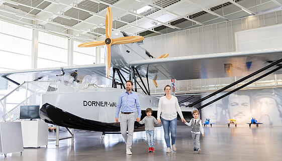 Eine Familie läuft durch die Ausstellung des Dornier Museums vor einem historischen Flugzeug Eine Familie läuft durch die Ausstellung des Dornier Museums vor einem historischen Flugzeug