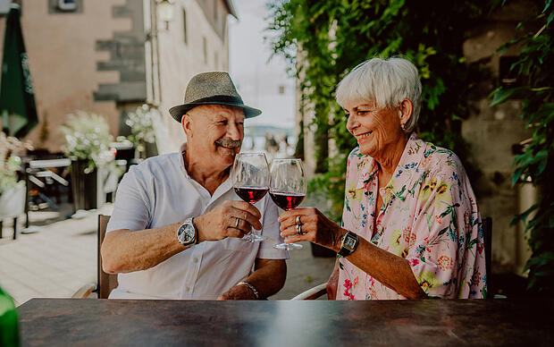 Älteres Ehepaar beim Anstoßen mit Rotweingläser am Bodensee im Sommer Älteres Ehepaar beim Anstoßen mit Rotweingläser am Bodensee im Sommer