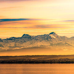 Bodensee und Alpenpanorama bei Sonnenuntergang und rötlichem Himmel