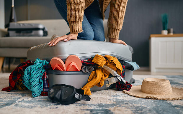 Frau versucht, einen vollgestopften Koffer zu schließen Frau versucht, einen vollgestopften Koffer zu schließen