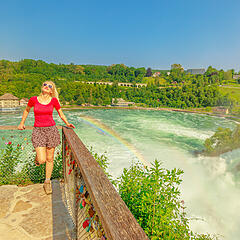 Junge Frau am Rheinfall in Schaffhausen bei Sonnenschein und Regenborgen