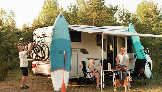 A happy family is resting nearby near their motorhome in the forest