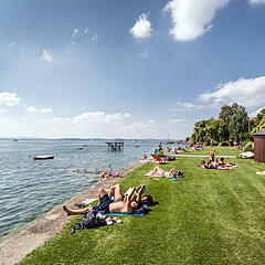 Menschen sonnen sich im Strandbad Meersburg auf einer Grasfläche direkt am Bodenseeufer Menschen sonnen sich im Strandbad Meersburg auf einer Grasfläche direkt am Bodenseeufer