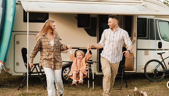 a young family is resting near their mobile home. Dad, mom and daughter play near the motorhome