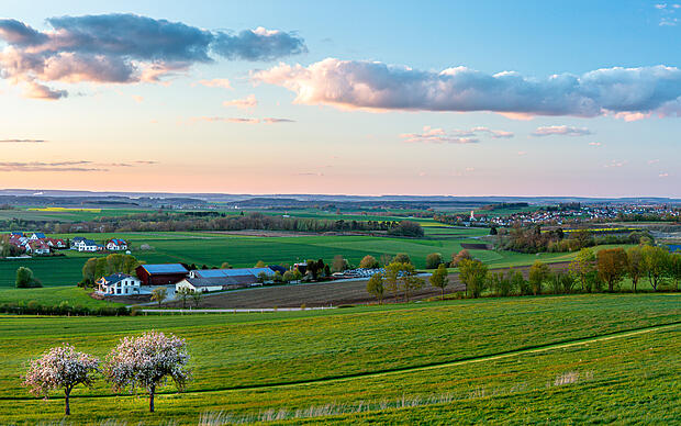 Oberschwäbische Kulturlandschaft in der Abendsonne mit Wiesen, Feldern Bäumen und einem Dorf Oberschwaben-Allgäu