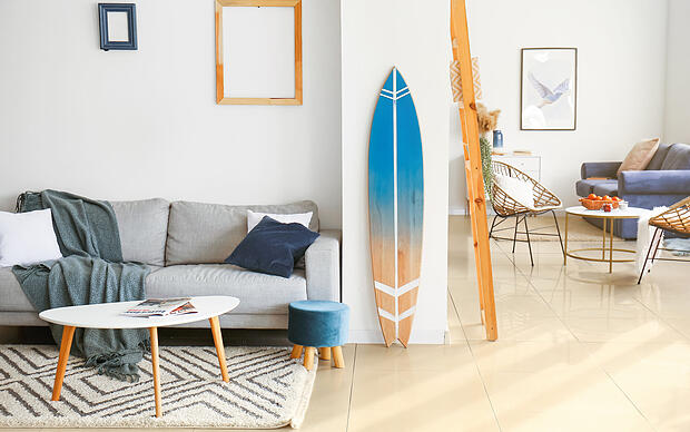 Blick ins Wohnzimmer einer Ferienwohnung auf ein an der Wand gelehntes Surfboard Blick ins Wohnzimmer einer Ferienwohnung auf ein an der Wand gelehntes Surfboard