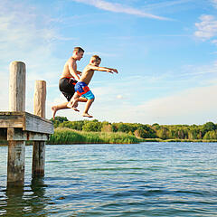 Zwei Kinder springen beim Baden von einem Pfahl-Steg in den See Zwei Kinder springen beim Baden von einem Pfahl-Steg in den See