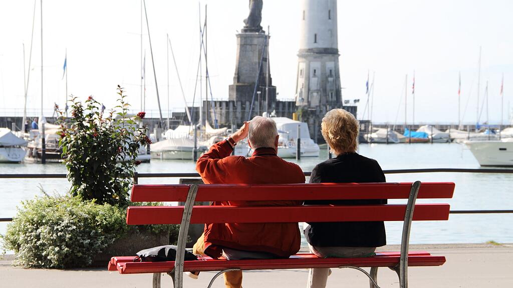 Älteres Ehepaar auf Parkbank beobachtet die Sehenswürdigkeiten am Hafen in Lindau Älteres Ehepaar auf Parkbank beobachtet die Sehenswürdigkeiten am Hafen in Lindau