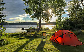 Camping mit rotem Zelt direkt am Seeufer bei Sonnenuntergang
