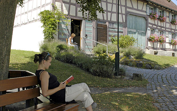 Frau sitzt vor dem Herrmann-Hesse-Museum auf der Halbinsel Höri und liest ein Buch